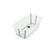 A clear plastic baby bathtub with sage green trim and a black drain plug sits at an angle, ready for bath time. 
